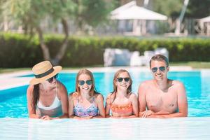 Happy family of four in outdoors swimming pool photo