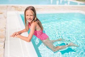 Adorable little girl swimming at outdoor swimming pool photo
