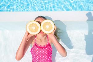 Little girl with halves citrus lemons in swimming pool photo