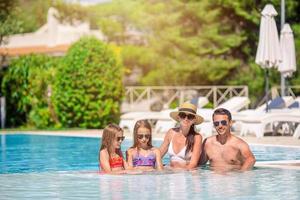 Happy family of four in outdoors swimming pool photo