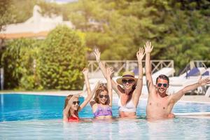 Happy family of four in outdoors swimming pool photo