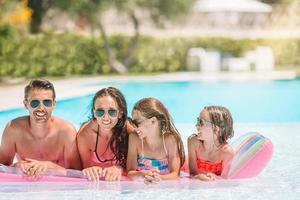 Happy family of four in outdoors swimming pool photo