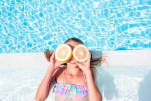 Little girl with halves citrus lemons in swimming pool photo