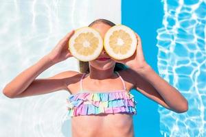 Little girl with halves citrus lemons in swimming pool photo