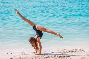 Active little girl at beach having a lot of fun. Cute kid making sporty exercises on the seashore photo