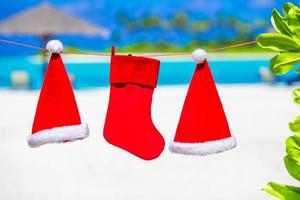 Red Santa hats and Christmas stocking hanging on tropical beach photo