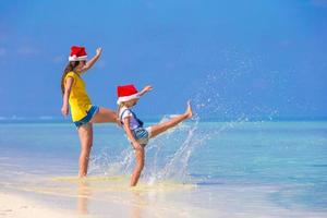 niña y madre joven con sombrero de santa durante las vacaciones en la playa foto