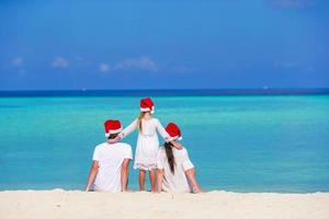 familia feliz con sombreros de santa en la playa durante las vacaciones de navidad foto