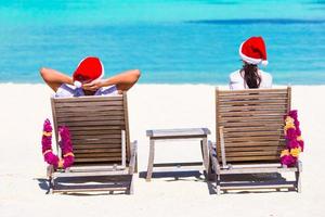 Young couple in Santa hats relaxing on beach during Christmas vacation photo
