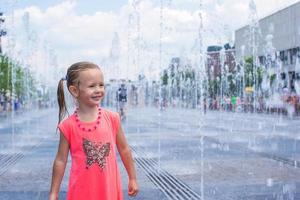 Little happy girl have fun in street fountain at hot sunny day photo