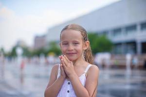 la niña se divierte en la fuente de la calle abierta en el caluroso día de verano foto