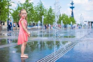 Little adorable girl have fun in street fountain at hot sunny day photo