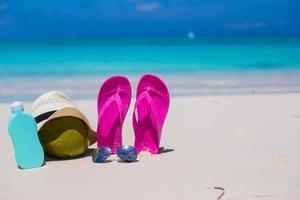 Flip flops, coconut, hat and suncream on white sand photo