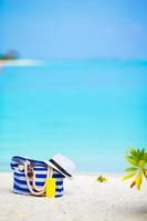 Beach accessories - blue stripe bag, straw hat, sunglasses on white beach photo