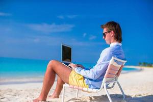 Young man working on laptop at tropical beach photo