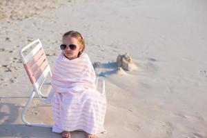 adorable niñita con gafas de sol cubierta con una toalla en la playa tropical foto