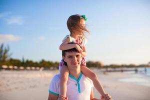 Little cute girl riding on her dad walking by the beach photo