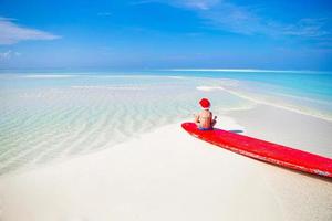 Little girl in Santa hat on white beach during Chrismas vacation photo