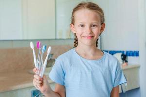 Little beautiful girl with white teeth with toothbrushes in hands in the bathroom photo