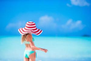 Adorable little girl in big hat walking along white sand Caribbean beach photo