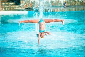 Happy little girl enjoy vacation in the swimming pool. Sporty kid making cartwheel on the edge of pool photo