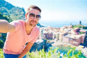 Young tourist in sunglasses taking selfie with scenic view of Vernazza, Cinque Terre, Liguria, Italy photo