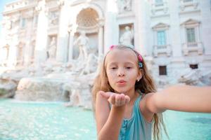 adorable niña tomando selfie junto a la fuente de trevi en roma. foto