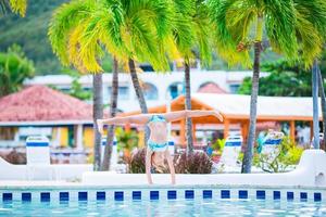 Happy little girl enjoy vacation in the swimming pool. Sporty kid making cartwheel on the edge of pool photo
