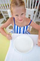 Adorable little girl having breakfast at outdoor summer cafe photo