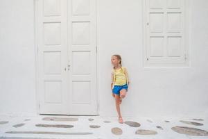 Little girl portrait outdoors in old greek village. Kid at street of greek village with white walls and colorful doors photo