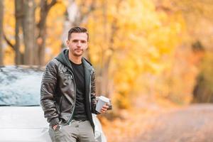 joven bebiendo café con teléfono en el parque de otoño al aire libre foto