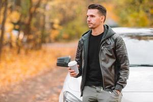 joven bebiendo café con teléfono en el parque de otoño al aire libre foto