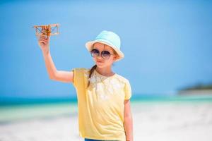 Happy child girl playing with toy airplane on the beach. Kid dream of becoming a pilot photo