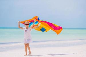 Happy little girl having fun running with pareo on tropical white beach photo