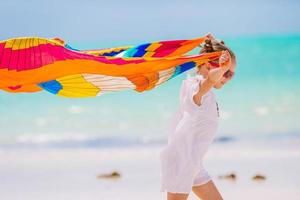 Happy little girl having fun running with pareo on tropical white beach photo