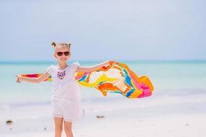 niña feliz divirtiéndose corriendo con pareo en playa blanca tropical