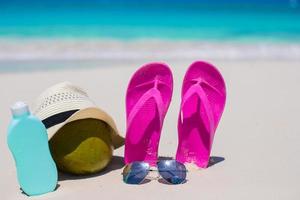 Flip flops, coconut, hat and suncream on white sand photo