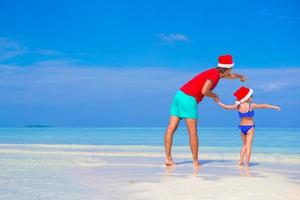 niña y padre feliz en sombrero de santa durante las vacaciones de navidad en la playa foto