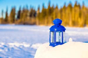 Blue lantern with a candle on white snow outdoors photo