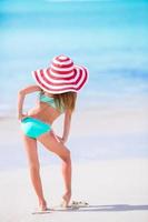 Adorable little girl in big hat walking along white sand Caribbean beach photo