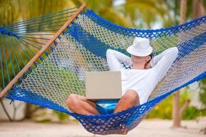 Young man with laptop at hammock on tropical vacation photo