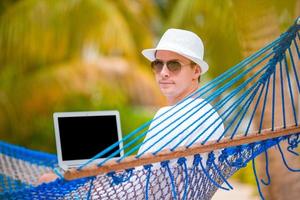 Young man with laptop at hammock on tropical vacation photo