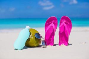 Flip flops, coconut and suncream on white sand photo