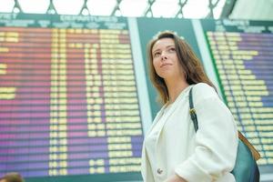 mujer joven en el aeropuerto internacional mirando el tablero de información de vuelo comprobando el vuelo
