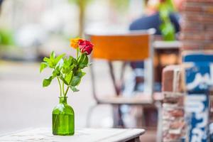 Glass vase with a flower on the table at outdoor restaurant photo