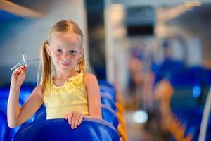 Adorable little girl traveling on train and having fun with airplane model in hands photo