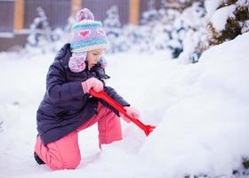 niña adorable juega con palas de nieve en el día de invierno foto