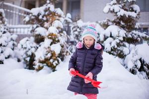 niña adorable juega con palear nieve en el día de invierno foto