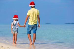 niña y padre feliz en sombrero de santa durante las vacaciones de navidad en la playa foto