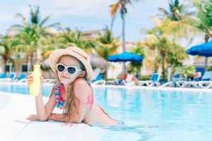 Little girl with bottle of sun cream in swimming pool photo